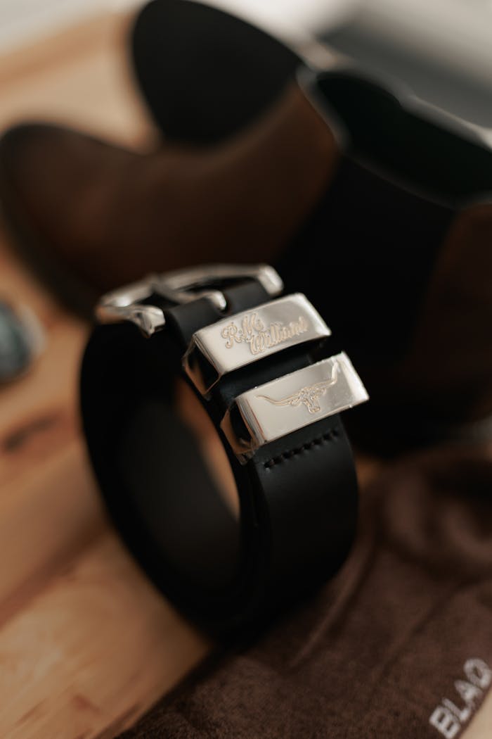 Close-up shot of a sleek black leather belt with a silver buckle alongside brown leather boots.