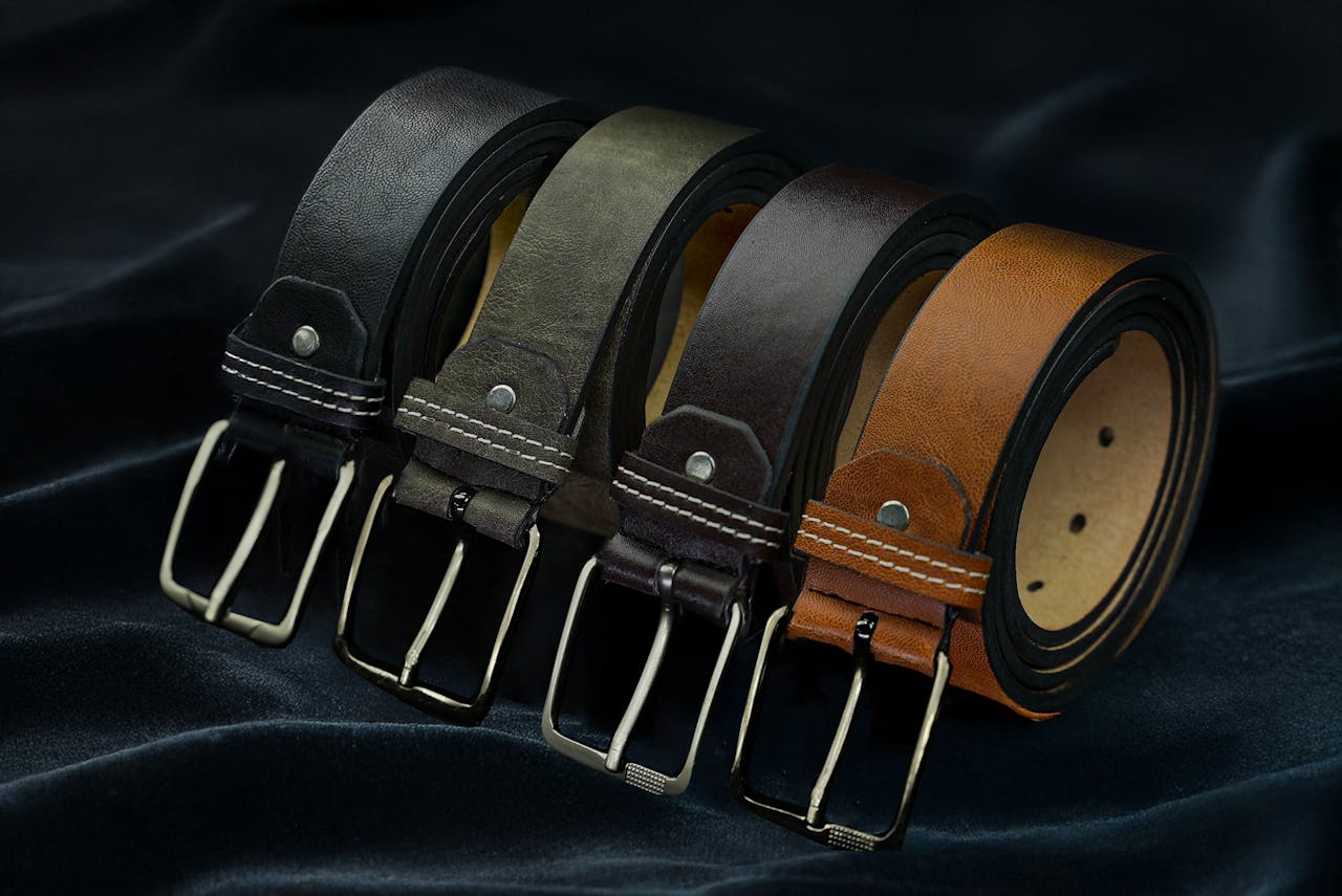 Set of luxurious leather belts in black, grey, brown, and tan on elegant fabric background.